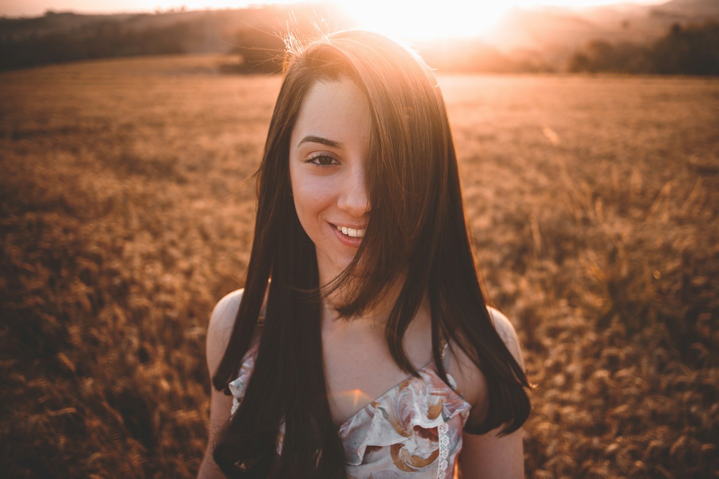 Frau mit langen dunklen Haaren lächelt in einem goldenen Feld.