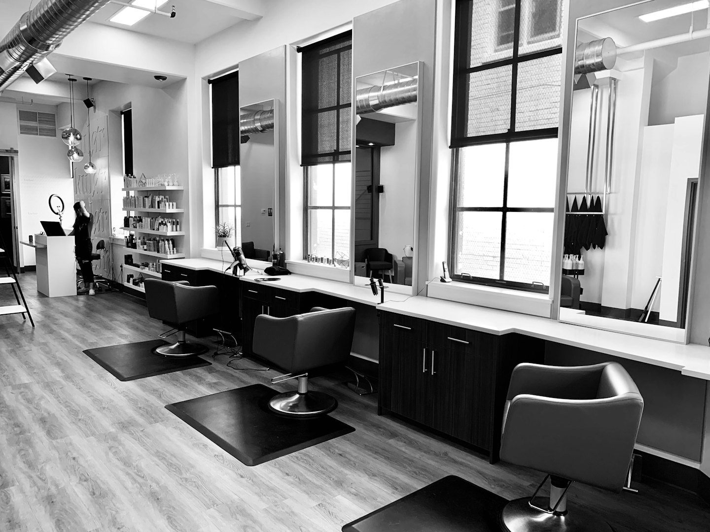 Moderner Friseursalon mit Friseurstühlen und einer Person am Tresen.
